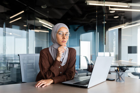 Portrait of a young successful Arab businesswoman in a hijab sitting in the office at a table and...