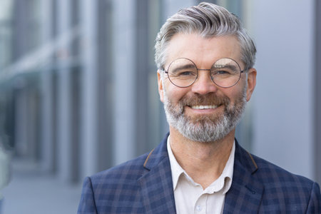 Successful gray haired man in business suit close up, portrait of mature businessman with beard and glasses, banker investor smiling and looking at camera from outside office building boss satisfied.の写真素材