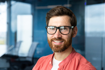 Close-up portrait of young businessman in red shirt, mature man in glasses smiling and looking at...