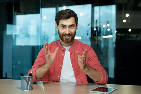 A young male teacher teaches online, conducts lectures, lessons. Sitting in the office at the table...