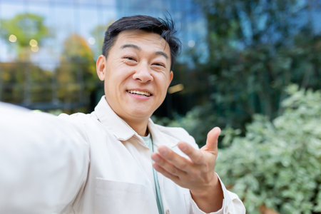 Close-up photo. A young male Asian student is standing outside the campus and talking on a video call. Takes selfies, records on video, podcast, blogger.の写真素材