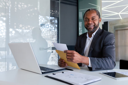 Portrait of successful african american businessman financier at workplace inside office building, male mature adult smiling and looking at camera, boss received mail envelope message.の写真素材