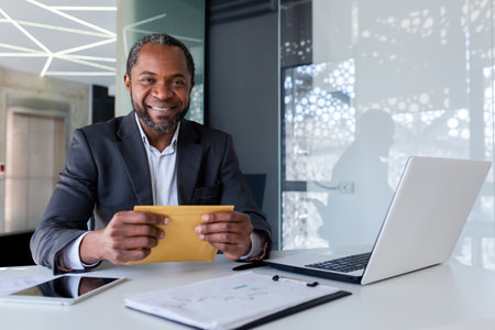 Portrait of successful african american businessman financier at workplace inside office building, male mature adult smiling and looking at camera, boss received mail envelope message.の写真素材