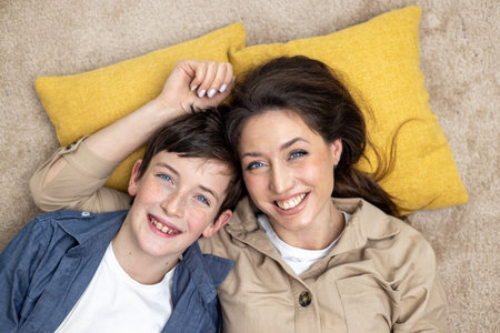 Portrait of happy woman with son, mother and boyfriend smiling and looking at camera lying together on carpets on floor at home in living room, having fun together.の写真素材