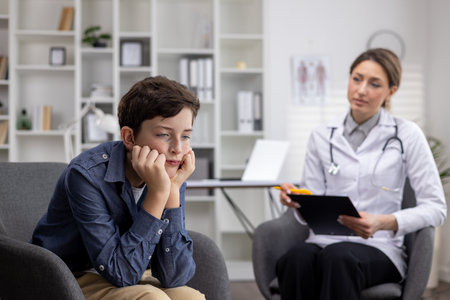 Admission of a young upset teenage boy to a pediatrician, a female doctor asks a young teenager about the disease, writes down information.の写真素材