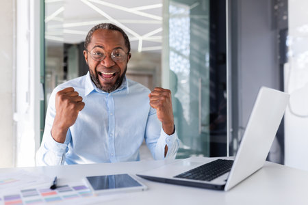 Portrait of satisfied broker investor, african american man smiling and looking at camera, mature businessman holding hands up celebrating success, workplace boss satisfied with achievement results.の写真素材