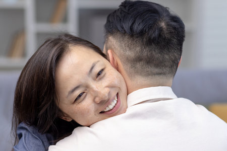 Close-up photo. Young Asian couple, family hugging together. Happy face of young woman hugging and supporting her husband, meets smiling at home.の写真素材