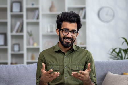 Video call online conversation, Indian man sitting on sofa at home, looking at web camera smiling and talking with colleagues friends remotely.の写真素材