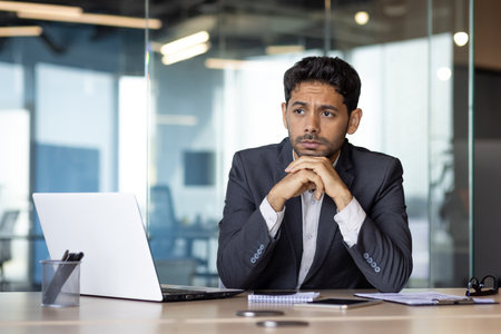 Serious thinking arab businessman at workplace, man sitting at desk with laptop in business suit, concentrating on solving financial problems.の写真素材