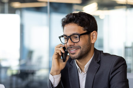 Young successful arab businessman boss talking on phone close up, man smiling contentedly inside office at workplace in business suit.の写真素材