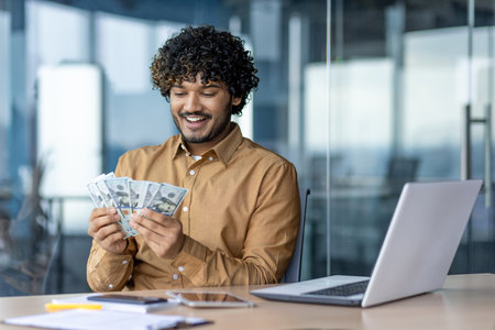 Young successful businessman at workplace, man holding cash money american dollars in hands, happy with good results of achievement at work in middle of office.の写真素材