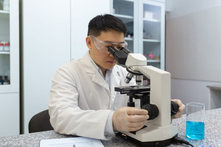 Young Asian male scientist, doctor working in laboratory under microscope, studying and researching...