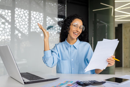 Happy and successful woman financier on paper work, satisfied with the results of the achievement, happy businesswoman holding papers, contracts and bills reports, hispanic woman inside the office.の写真素材
