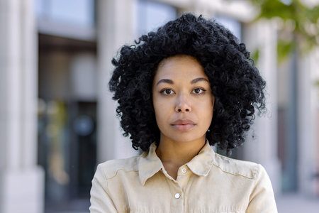 Close-up portrait of young serious thinking woman outside office building, business woman with curly hair looking at camera.の写真素材