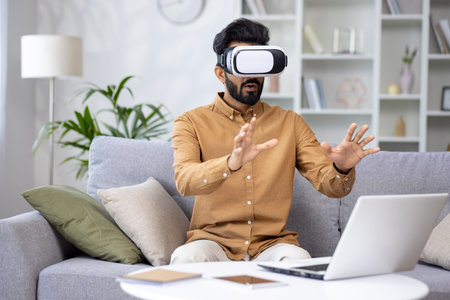 Surprised serious man in virtual reality glasses reviewing course in virtual meeting sitting on sofa...