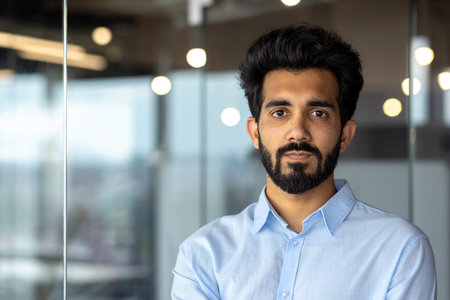 Close-up photo. Portrait of a young Indian businessman man wearing a blue shirt standing in the office and seriously looking at the camera.の写真素材