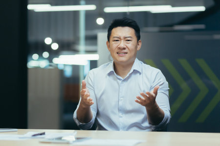 Angry and displeased young asian man businessman, office worker talking emotionally to camera on...