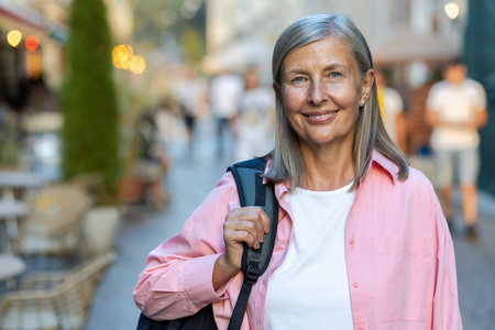 Close-up photo. Portrait of a beautiful senior woman in a pink shirt holding a backpack on her...