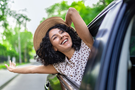 Young girl traveling by car, hispanic woman with curly hair looking out the window, enjoying vacation and travel.の写真素材