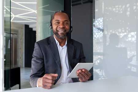 Portrait of support worker inside office at workplace, man smiling and looking at camera, using...