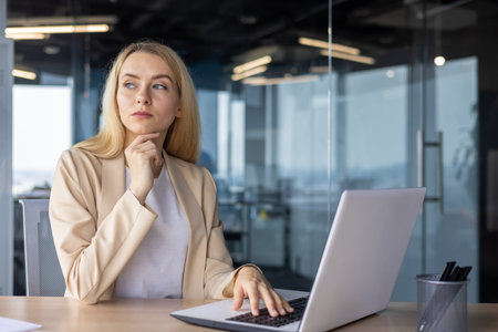Serious concentrated thinking woman at workplace inside office working with laptop, businesswoman brainstorming strategy plans financial tasks.の写真素材