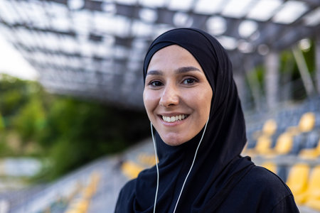 Portrait of happy muslim woman in hijab and headphones on court, doing sports and listening to music, smiling and looking at camera.の写真素材