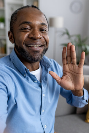 Vertical close-up photo of a young African-American man talking to the camera on a video call, recording, waving and greeting.の写真素材
