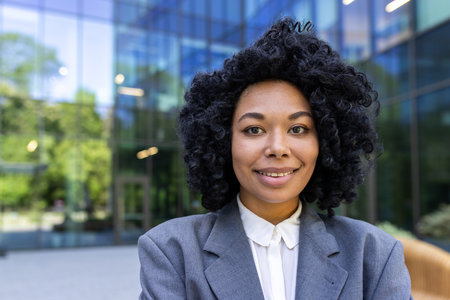 Close-up portrait of successful young business woman, female worker outside office building smiling and looking at camera, African American woman smiling contentedly in business clothes.の写真素材