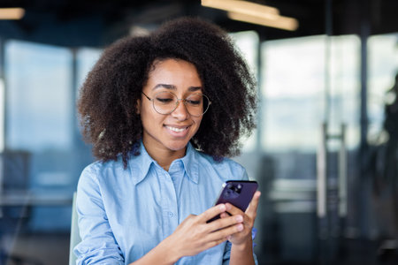 Close-up photo of a young smilling African-American woman in an office using a mobile phone.の写真素材