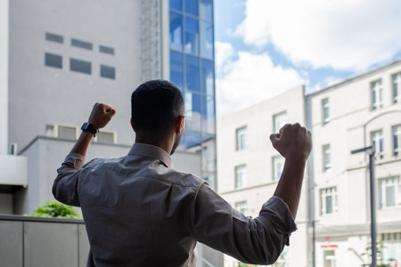 Energized African American young man in shirt showing victory gesture, feeling triumphant near...