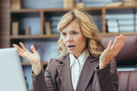 An exasperated mature female executive experiences trouble while working from her stylish home office setting.の写真素材