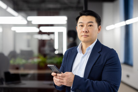 Portrait of serious concentrated businessman asian, man with phone in hands looking at camera,...