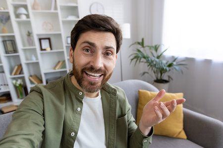 Cheerful mature man with beard taking a selfie in his well-decorated living room, radiating...
