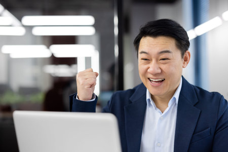 Asian man celebrating victory success, businessman in business suit happy with achievement results...