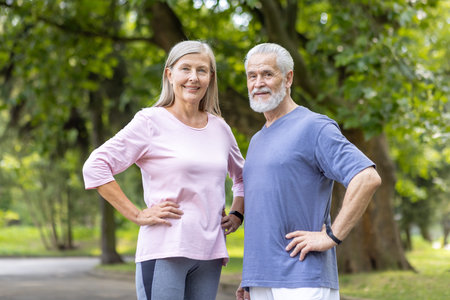A smiling mature couple in sportswear poses confidently during a fitness session in a serene park...