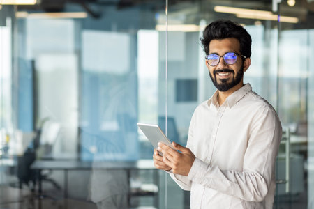 Portrait of a successful Indian young male programmer engineer wearing glasses standing inside the...