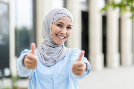 A cheerful, young woman wearing a hijab gives a double thumbs up with a broad, confident smile, signaling approval and success.の写真素材