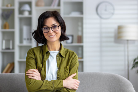 A cheerful woman with glasses in a home office setup exudes confidence and professionalism while smiling.の写真素材