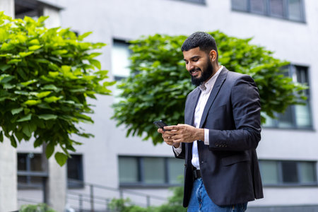 A young, smartly dressed businessman engages with his smartphone while standing outdoors. The image encapsulates themes of connectivity, entrepreneurship, and modern communication.の写真素材