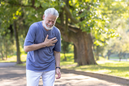 Senior gray-haired man suffering from a heart attack after walking and playing sports, standing in...