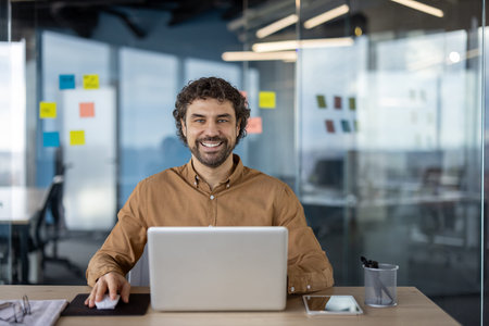 Portrait of a cheerful Hispanic businessman looking at the camera while working on his laptop in a...