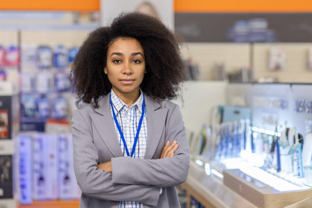 A confident businesswoman with an afro in an electronics store is ready to assist customers, dressed professionally in business casual with a lanyard, showcasing technology expertiseの写真素材
