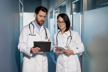 Medical professionals discussing patient records in hospital corridor. Man and woman in white coats...