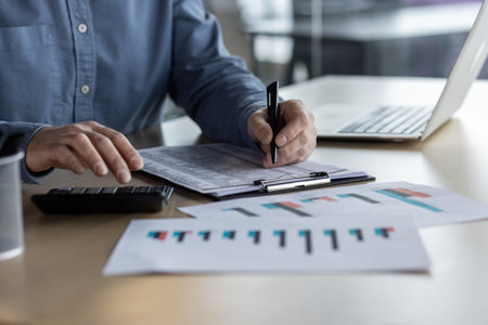 Business professional analyzing financial charts and graphs at desk. Hands holding pen and...