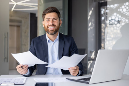 Portrait of a happy young office worker man, a businessman sitting at a desk in a suit, smiling and...
