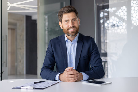A professional middle-aged businessman smiles confidently at the camera, dressed in a smart blue...