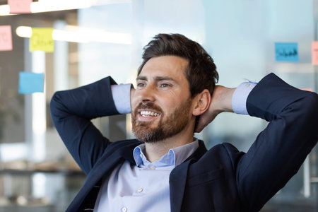 Confident business man sitting at desk in office, smiling with hands behind head. Achieved success...