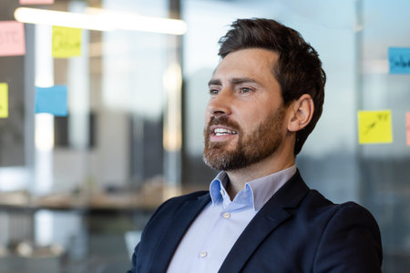 Confident business professional in modern office setting with colorful sticky notes on glass wall....