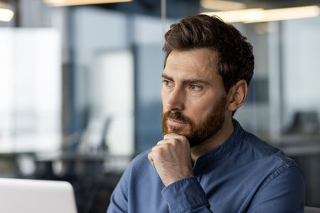A serious young man businessman, director and boss sits in the office at a workplace with a laptop...