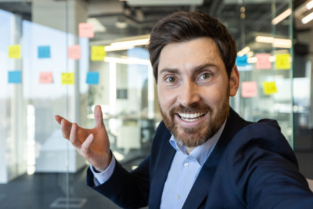 Confident businessman smiling and making gesture while on video call using phone in modern office....
